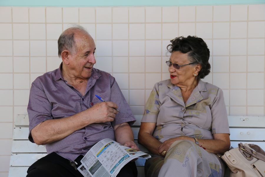 Casal de aposentados conversando e sorrindo num banco, em Brasília